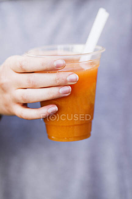 Una mano sosteniendo una taza de jugo de fruta fresca prensada - foto de stock