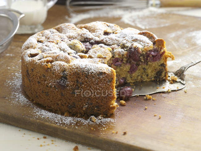 Cherry cake dusted with icing sugar, a piece cut — Stock Photo