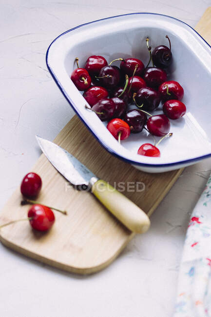 Cerejas estanho cerâmico e em tábua de madeira com faca — Fotografia de Stock