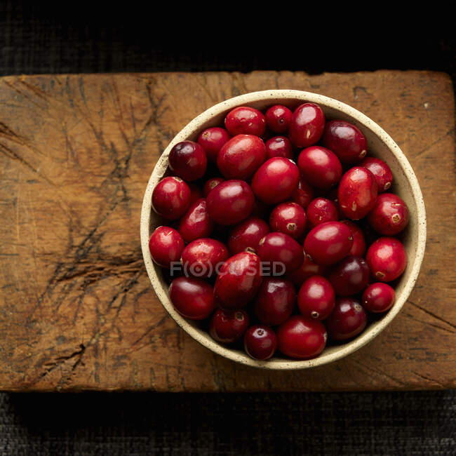 Cranberries em tigela na placa de corte de madeira — Fotografia de Stock