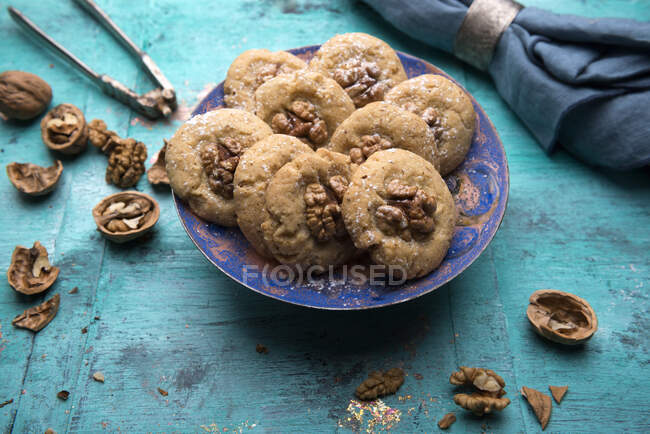 Cookies with walnuts halves in plate with cloth napkin, nuts and cracker on blue surface — Stock Photo