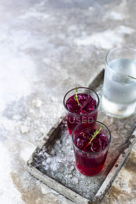 Свекла джин в стаканах со льдом и тимьян на металлическом подносе с кувшином холодной воды — стоковое фото