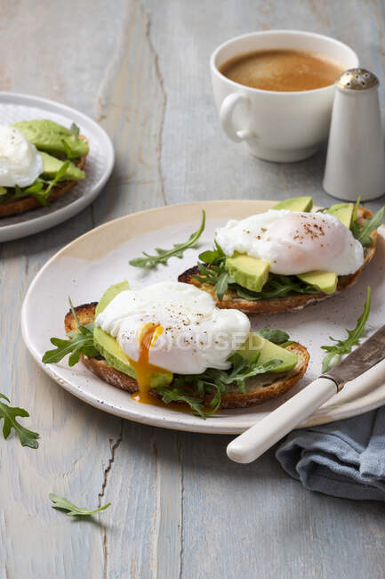 Toasts with avocado, rocket and poached eggs, coffee, rocket leaves — Stock Photo