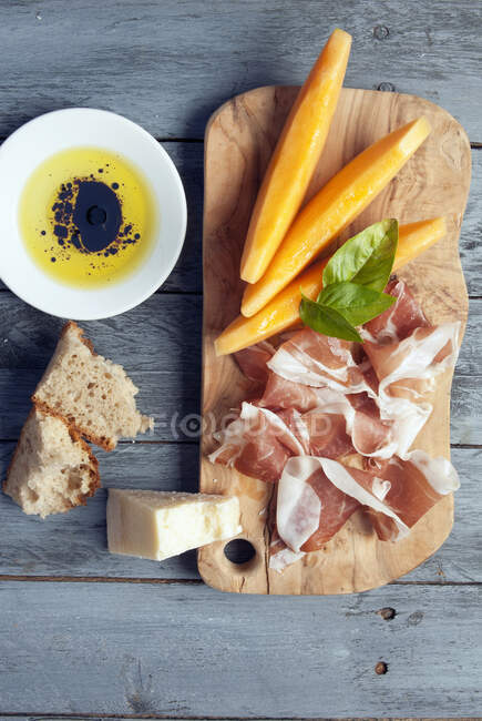 Antipasto prosciutto and organic melon with bread and basil leaves — Stock Photo