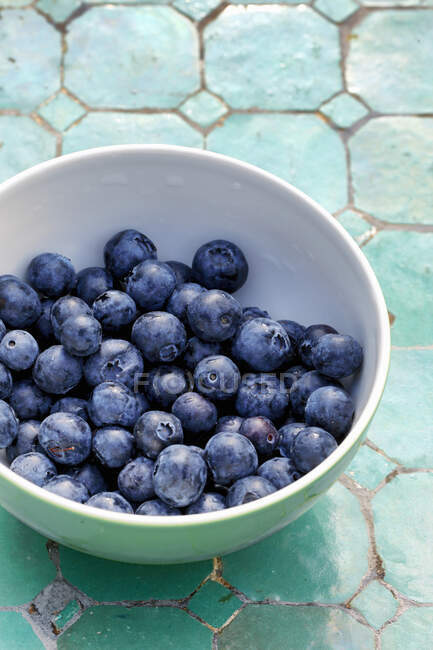 Blueberries in ceramic bowl on blue tiles — Stock Photo