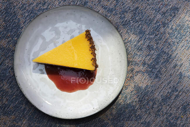 Una rebanada de tarta de mango con crema de yogur, una base de galletas y salsa de bayas - foto de stock