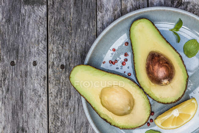 Fresh halved avocado with lemon wedge and mint leaves — Stock Photo