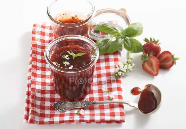 Engarrafamento de morangos em jarros com folhas de manjericão frescas e flores — Fotografia de Stock