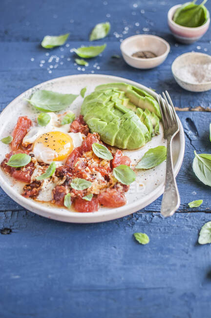 Egg cooked in tomato sauce served with fresh basil and avocado — Stock Photo