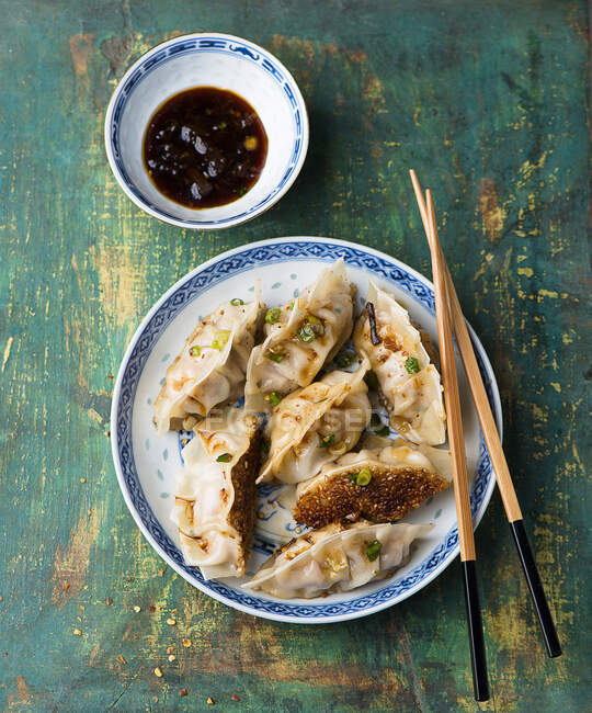 Китайские пельмени с палочками на тарелке и соусом в миске — стоковое фото
