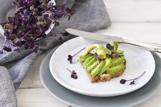 Whole grain bread topped with avocado and sprouts — Stock Photo