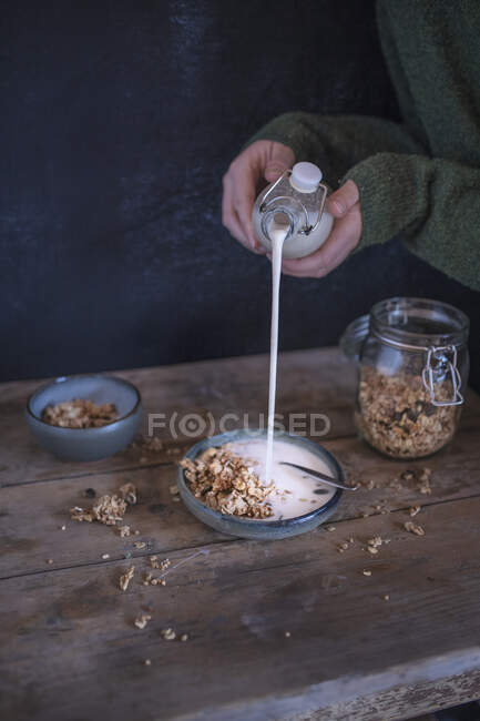 Uma pessoa derramando leite em uma tigela de muesli — Fotografia de Stock