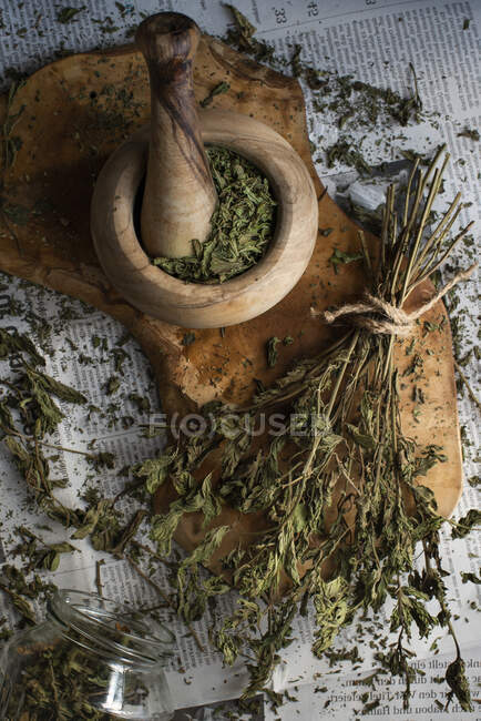 La menta seca en un mortero de madera de olivo sobre una tabla de madera en el periódico - foto de stock