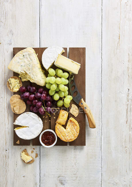 Selection of soft cheeses with biscuits, grapes and chutney on brown wooden board — Stock Photo