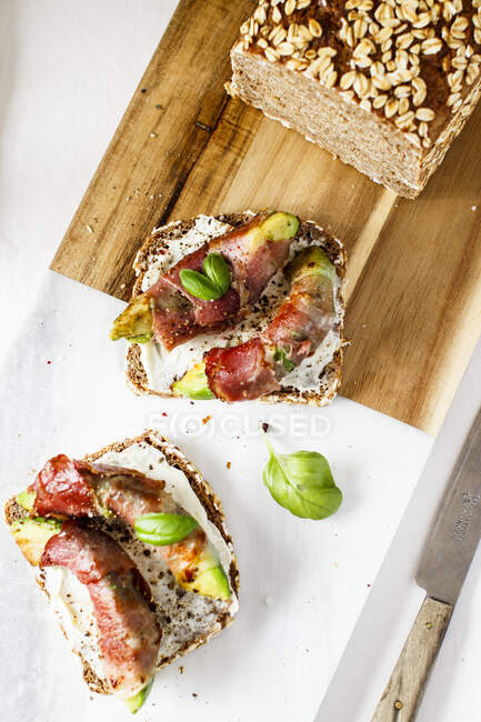 Brotscheiben mit Frischkäse, Avocado und Speck belegt — Stockfoto