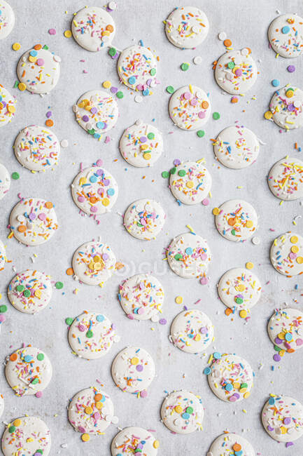 Macarons halves with colorful sprinkles on baking paper — Stock Photo