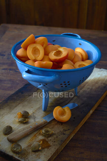 Свіжі навпіл абрикоси в синій друшляк на дерев'яній поверхні з ножем — стокове фото