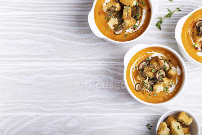 Tre ciotole di ceramica bianca con crema di zucca purea di zuppa con funghi, crostini e panna pesante — Foto stock
