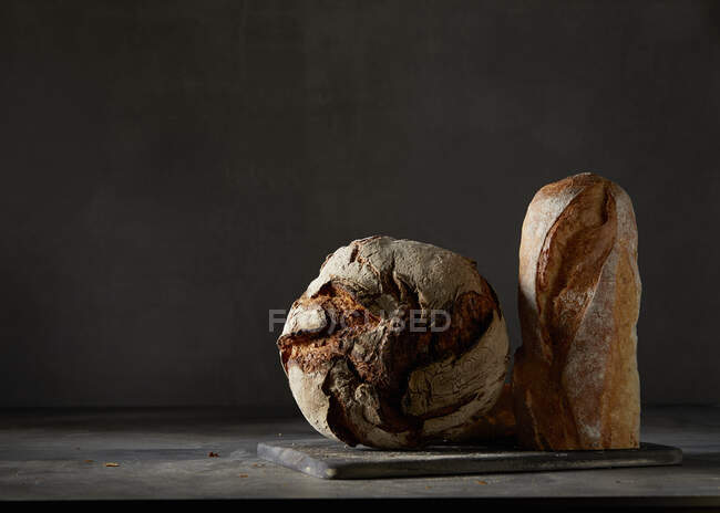 Pan crujiente y una baguette frente a un fondo oscuro - foto de stock