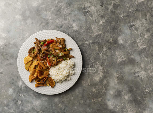 Lomo saltado - Peruvian beef tenderloin with red onions, yellow chili, tomatoes, with potato fries and rice — Stock Photo