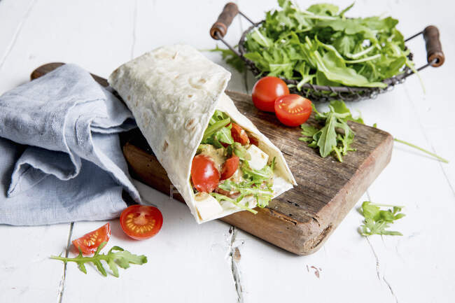 Wrap with tomatoes, mozzarella and rocket salad on wooden board — Stock Photo