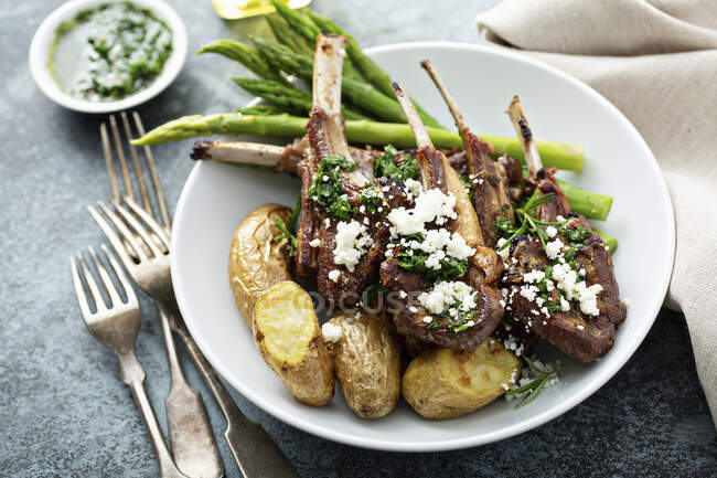 Grilled lamb chops with green herb sauce, feta, asparagus and potatoes served on wooden board — Stock Photo