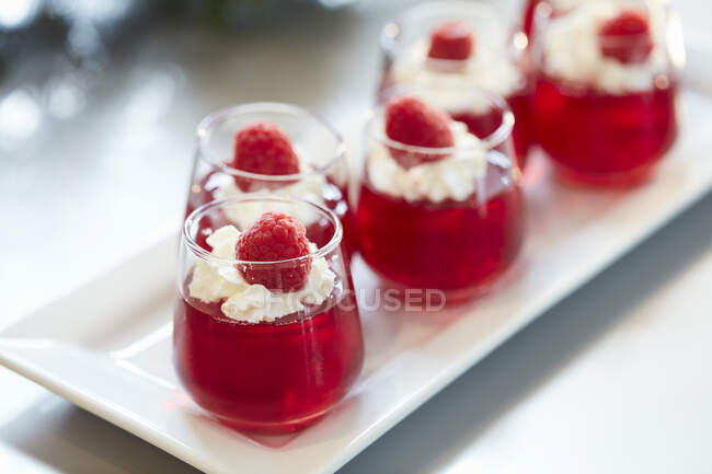 Jelly glass shots with whipped cream and fresh raspberries — Stock Photo