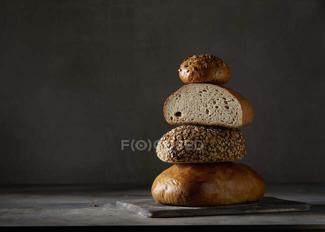 Drei Brote und ein Brötchen, gestapelt vor dunklem Hintergrund — Stockfoto