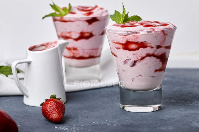 Клубничный мусс в стаканах, сироп в кувшине и свежая ягода на столе — стоковое фото
