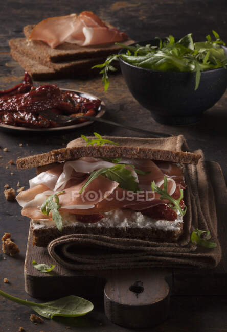 Jamón curado en pan con queso de cabra, cohete y tomates secos - foto de stock
