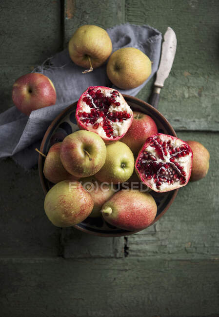 Apples, pears and pomegranate in a bowl on a green wooden surface — Stock Photo