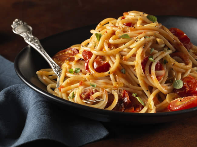 Паста Спагетті з помідорами та травами в чорній мисці з виделкою — стокове фото
