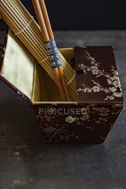 Una caja de seda oriental con una estera de bambú y palillos - foto de stock