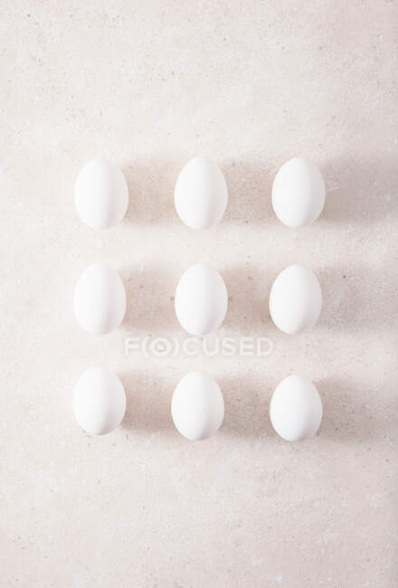 Nueve huevos blancos en filas en la superficie de piedra - foto de stock