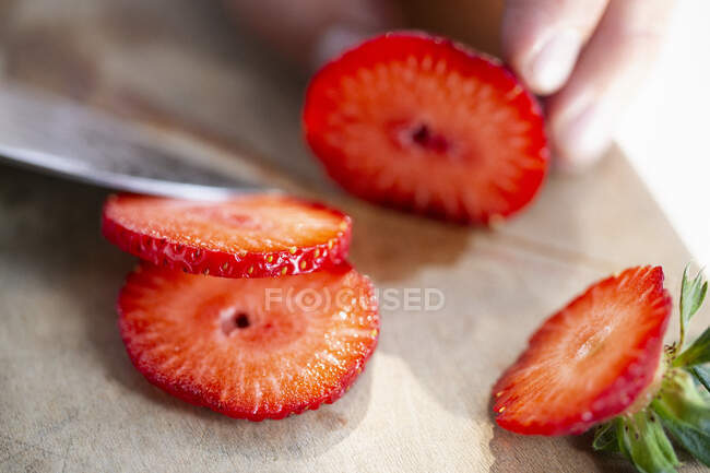 Dedos segurando morango e cortando-o com faca na tábua de madeira — Fotografia de Stock