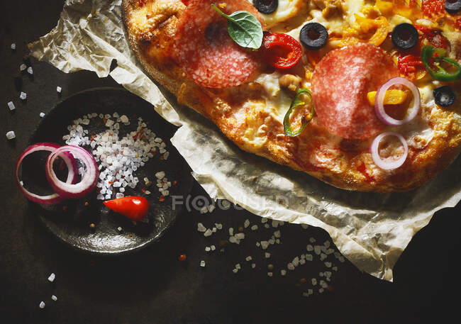 A pizza topped with salami, olives, peperoni and onions (close-up) — Stock Photo