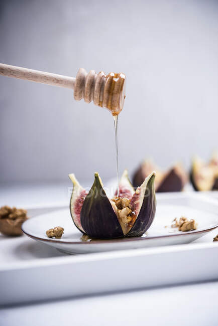 Baked fig filled with walnuts and almonds, honey dripping on fruit from wooden stick — Stock Photo