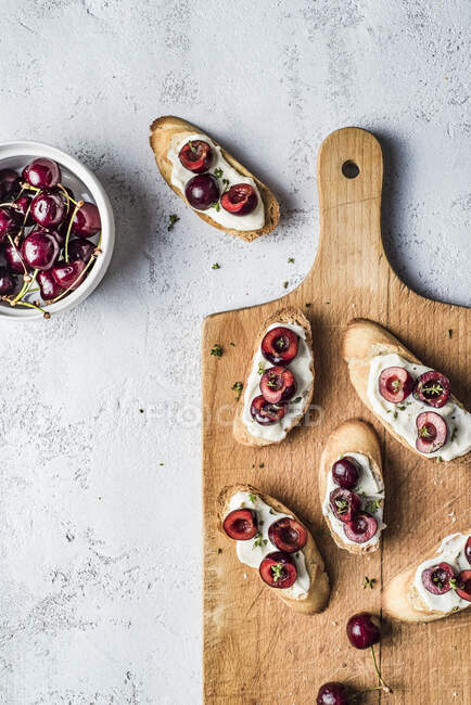 Fette di bruschetta con ciliegie, crema di mascarpone e timo su tavola di legno e bacche fresche in ciotola — Foto stock