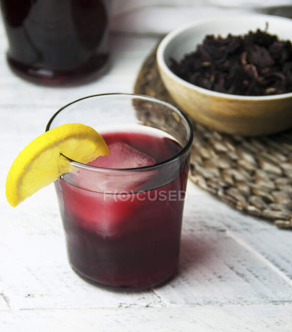 Стакан холодного соррельского напитка с лимонным клином, гарниром из листьев сорреля в миске — стоковое фото