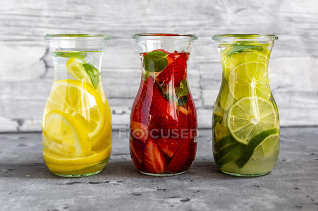 Bottles of Infused drinks with strawberries, lime and lemon — Stock Photo