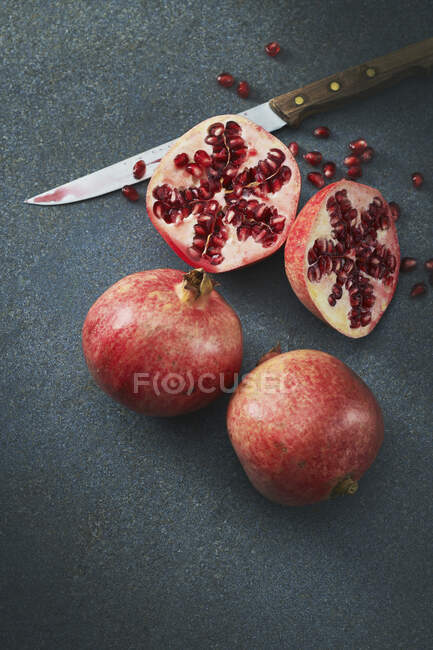 Pomegranates, whole and halved on table with knife — Stock Photo