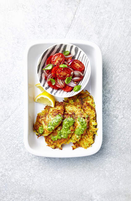 Potato and zucchini fritters served with green pesto and tomato salad — Stock Photo