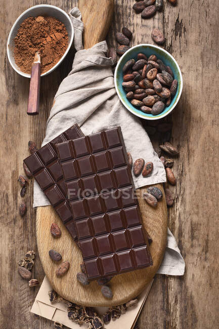 Bars of chocolate, cacao powder and cacao beans on wooden board — Stock Photo