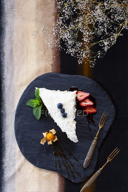 Ломтик кокосового пирога с ягодами и физалисом подается на тарелке — стоковое фото