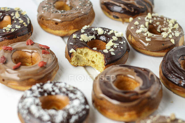 Varios donuts con glaseado de chocolate, uno con un bocado sacado - foto de stock