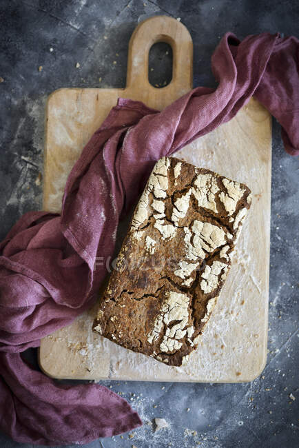 Sourdough bread in wholegrain flour on wooden board with cloth — Stock Photo