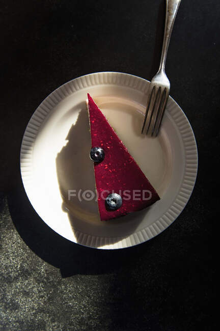 Un pezzo di torta di lamponi con due mirtilli su un piatto con una forchetta — Foto stock