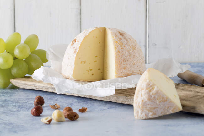Soft cheese on paper, hazelnuts and grapes — Stock Photo