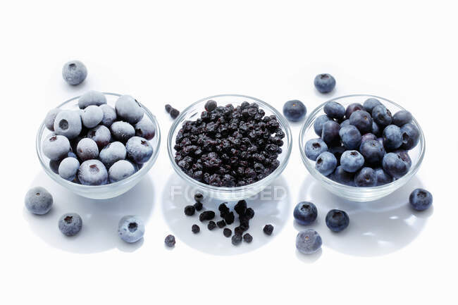 Blueberries: fresh, dried and frozen in bowls and on white surface with reflections — Stock Photo