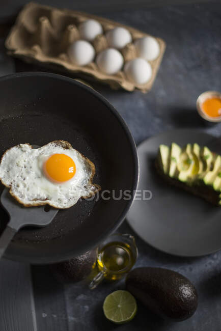 Un huevo frito en una sartén servido con aguacate fresco para el desayuno - foto de stock